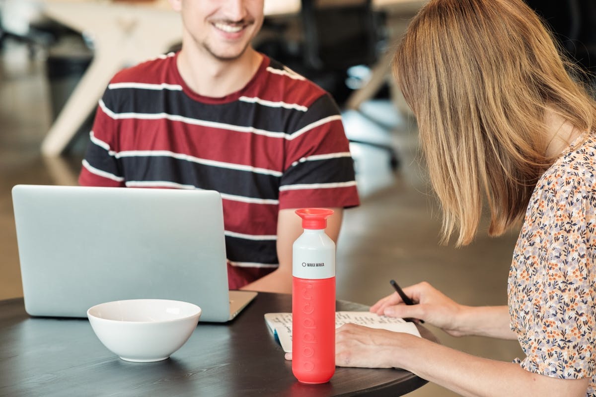 Two people with a laptop, a paper notebook and a red Dopper Original with the company logo on the cup