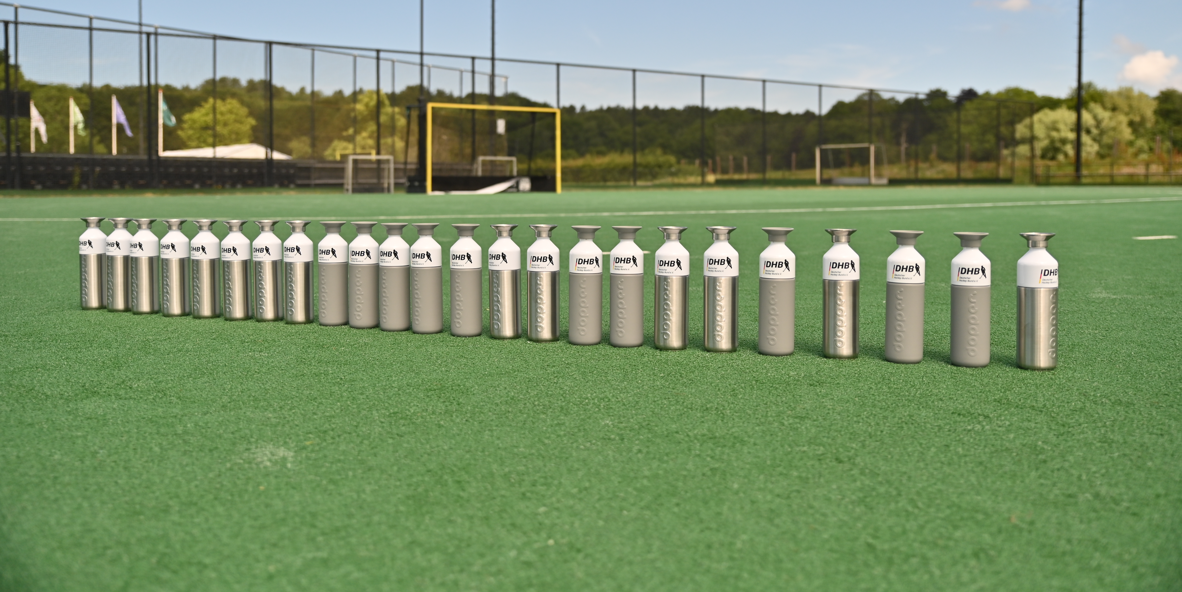 Line up of Steel and grey customised Dopper bottles on a field hockey field